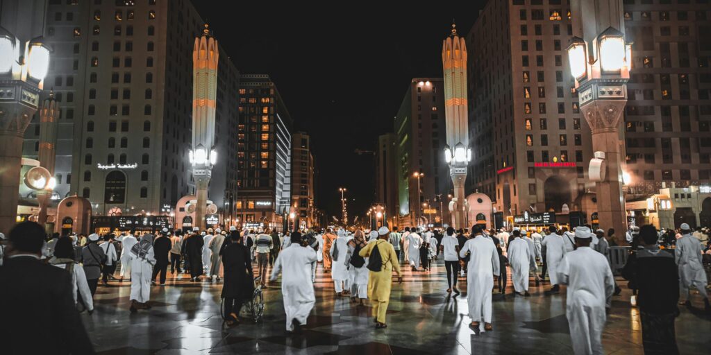 A busy street in Medina, Saudi Arabia, filled with people under illuminated city lights at night.