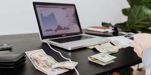 A workspace with cash, laptop, and financial graph showing investment analysis.
